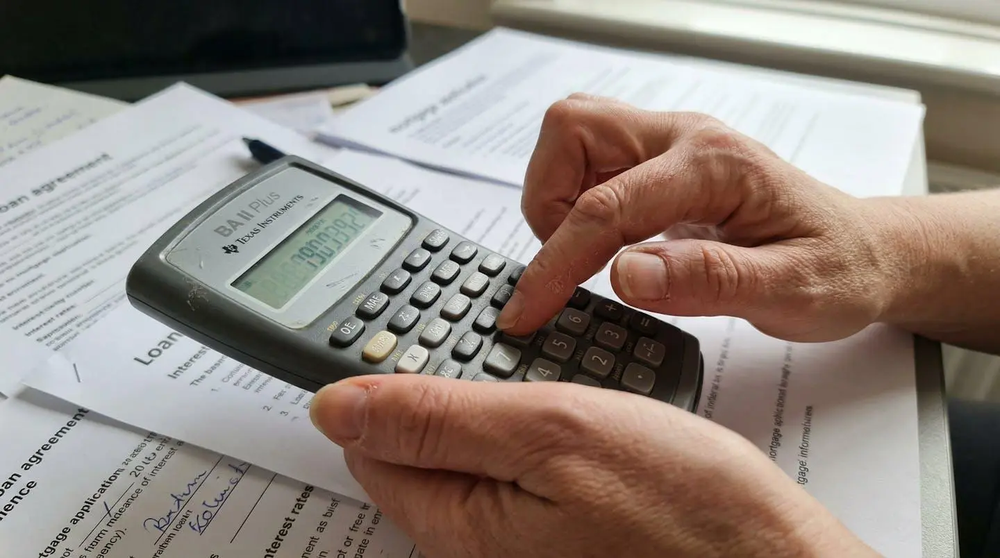 Des mains tapent sur une calculatrice financière avec des documents bancaires partiellement visibles en arrière-plan flou